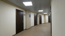 Empty, Round Corridor With Light Beige Walls And Closed, Dark Brown Doors. Closed Doors Along A Lighted Corridor In The Office Building.