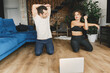 © shunevich - Young Caucasian sporty couple watching live or video tutorial practice sport lesson at home together. Healthy man and woman stretching and balancing body on floor. Sport lifestyle