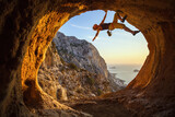 Fototapeta  - Young woman free solo climbing in cave with beautiful sea view in background