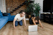 © shunevich - Beautiful curly-hair female trainer helps her boyfriend warm up at home during quarantine. Very emotional male sitting on the floor of modern apartment and hardly stretching. Healthy lifestyle