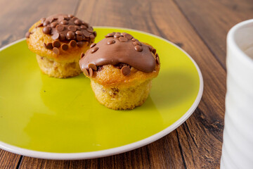 Two chocolate chip muffins on a yellow plate and wooden table . Copy space. Premium quality bakery product.