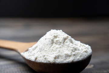 Whole flour in spoon on dark vintage wooden background. Close up view. Preparations for homemade baking. Basic ingredients for baking. 
Wheat flour on wooden spoon. 