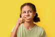 African-American teenage girl brushing teeth on yellow background