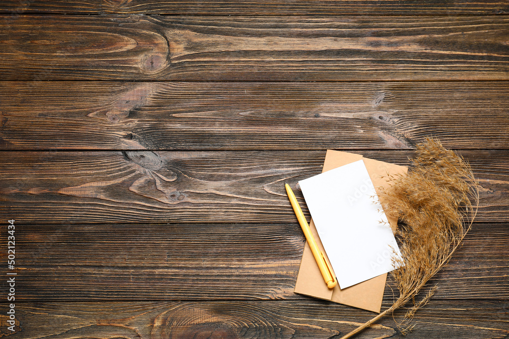 Envelope with blank card, pen and pampas grass on dark wooden background