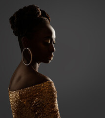 Wall Mural - African Woman Face Profile Black Silhouette. Dark Skin Beauty Model with Gold Ring Earrings and Afro Braids Hairstyle in Glitter Golden Dress over Gray Background in Backlight