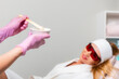 Beautician in pink medical gloves mix the epilation agent gel. Hands close up. Defocused woman client at the background. The concept of hair removal and epilation