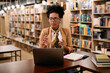 © Drazen - Black female teacher talks while holding online class over laptop from library.