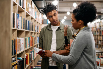Young African American student talks to librarian at university library,