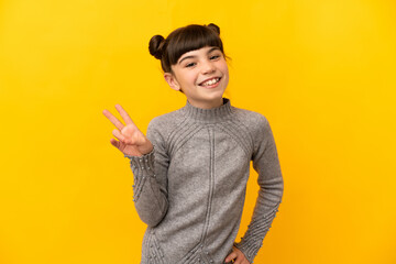 Wall Mural - Little caucasian girl isolated on yellow background smiling and showing victory sign