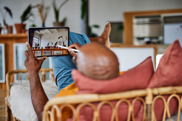 Bald man with digitized pen using tablet PC lying on sofa at home