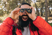 Cheerful Bearded Man With Mouth Open Looking Through Binoculars In Forest
