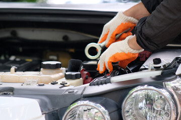 Hands of an automobile mechanic repairman with a wrench repairing a car engine at an automotive workshop, car servicing and maintenance, repair service.