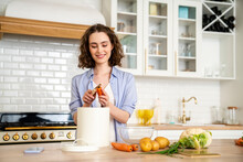 Smiling Woman Peeling Carrot At Dining Table In Kitchen