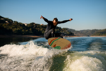 Athletic wakesurfer jumping on a wakesurf board over the river waves