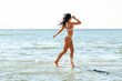 © Syda Productions - people, summer and swimwear concept - young woman in bikini swimsuit running in shallow water on beach