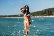 © Syda Productions - people, summer and swimwear concept - happy smiling woman in bikini swimsuit splashing sea water on beach