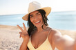 © Syda Productions - people, summer and swimwear concept - happy smiling young woman in bikini swimsuit and straw hat taking selfie on beach and showing peace gesture