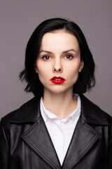 Wall Mural - brunette woman with red lipstick on her lips in a black leather jacket and white shirt, grey background