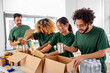 © Syda Productions - charity, donation and volunteering concept - international group of happy smiling volunteers packing food in boxes according to list on clipboard at distribution or refugee assistance center