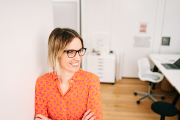 Young businesswoman with black glasses and red blouse looks sideways laughing