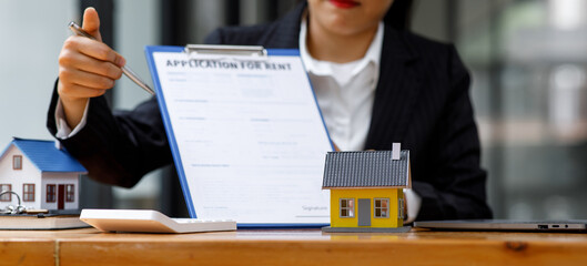 Businesswoman realtor taking notes and holding house model, sitting at desk with paper house model and keys, female real estate agent manager, preparing documents, mortgage and property.