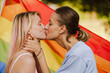 © Drobot Dean - Young lesbian couple with rainbow flag kissing during pride parade