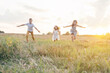 © Евгения Рубцова - Portrait of three children playing game of catch, jumping and running on dry grass hay field paths in sunset. Trees and meadow on background. Looking around. Cloudy sunny sky. Haying time