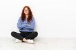 © luismolinero - Teenager redhead girl sitting on the floor isolated on white background keeping the arms crossed in frontal position
