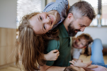 Cheerful father with three little daughters playing together at home.