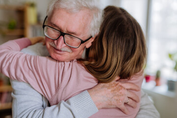 Rear view of adult daughter hugging her senior father when visitng him at home.