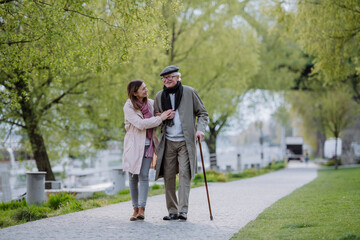 happy senior man with walking stick and adult daughter outdoors on a walk in park.