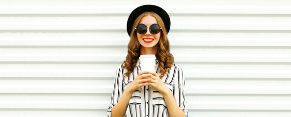 Portrait of happy smiling young woman drinking coffee wearing black round hat on white background