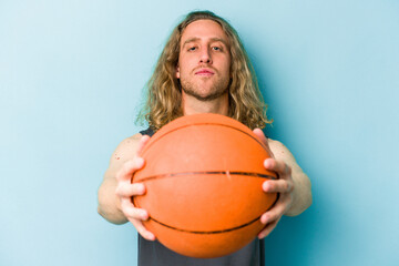 Wall Mural - Young caucasian man playing basketball isolated on blue background