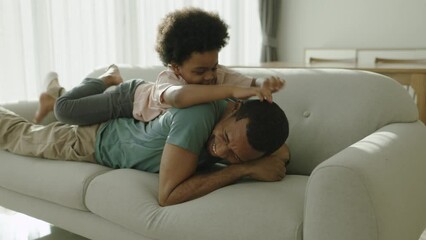 Wall Mural - Happy African Father and little Afro boy playing on sofa together, Smiling Dad embracing or cuddling his son