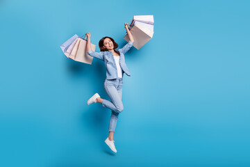 Wall Mural - photo of shiny pretty lady dressed denim shirt jumping high holding shopping bags isolated blue colo