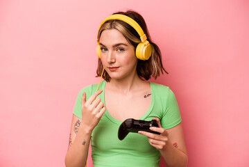 Young caucasian woman playing with a video game controller isolated on pink background pointing with finger at you as if inviting come closer.