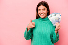 Young Caucasian Woman Holding Banknotes Isolated On Pink Background Smiling And Raising Thumb Up