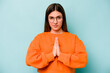 Young caucasian woman isolated on blue background praying, showing devotion, religious person looking for divine inspiration.
