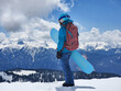 Young active woman with snowboard standing at snowy mountains background