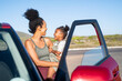Happy black mother holding little daughter outside car