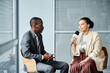 © Seventyfour - Portrait of young African American journalist speaking to microphone while interviewing businessman in studio