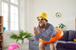 © Studio Romantic - Funny crazy man with inflatable circle pretends to be swimming at home in living room. Absurd chubby guy in striped swimsuit having fun with circle for swimming at waist imagining that he is on beach.