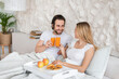© Prostock-studio - Happy millennial couple having breakfast in bed together, spending honeymoon at hotel, copy space