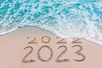 Wall Mural - message year 2022 replaced by 2023 written on beach sand background. good bye 2022 hello to 2023 hap