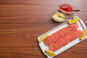 Wall Mural - Cambuí sausage, typical Brazilian snack, served with lemon slices, chili sauce and mayonnaise. on wooden table