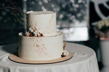 A wedding cake. Milk-colored cake decorated with cotton beads and gold leaf on a dark background in wedding day