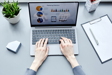 Top view closeup of young professional doing marketing research while using laptop and looking at data charts on screen