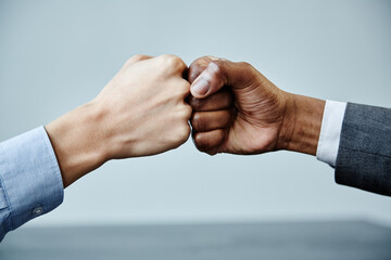 Close up of two business partners fistbumping in unity at meeting table, copy space