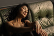 © Julia - Sexy brunette Asian woman in a bra and black pantyhose sits on a leather sofa indoors. A woman sensually dreams of her husband