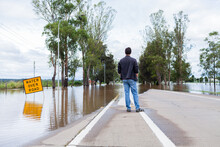 Person Looking At Floodwaters Over Road Cutting Off Access Via New England Highway Through Singleton